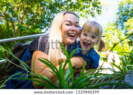 Cute blonde woman and her daughter have fun in the park. Family with happy emotion. Horizontal close up portrait little girl and her mom playing outdoor together
