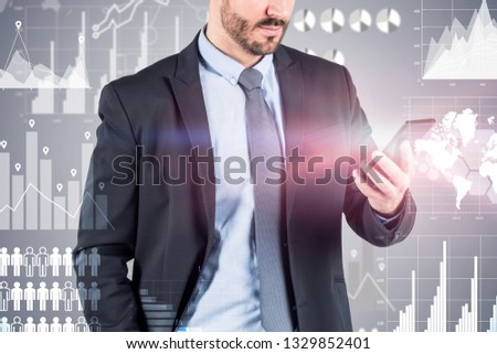 Unrecognizable young businessman with beard looking at his smartphone standing over gray background with business infographics. Double exposure Elements of this image furnished by NASA