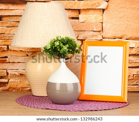 Colorful photo frame, lamp and flowers on wooden table on stone wall background