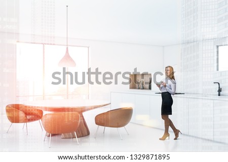 Woman in corner of modern kitchen with white walls and floor, large windows, white countertops and round table with leather armchairs. Toned image double exposure