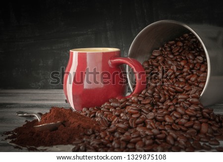 Coffee beans spilled out of a tin can onto a wooden table. Near the burgundy cup and freshly ground coffee. Photo in dark style.