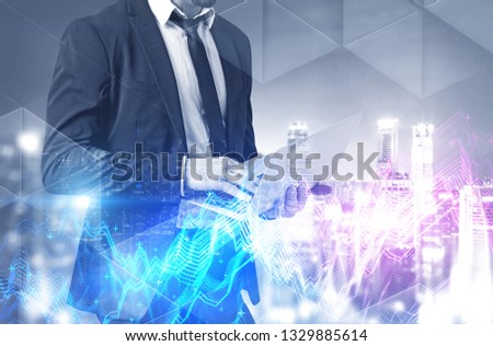 Portrait of unrecognizable businessman working with laptop over night cityscape background with double exposure of graphs. Toned image