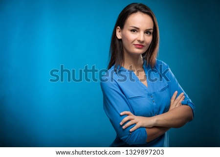 Pretty, young businesswoman with folded arms against blue background