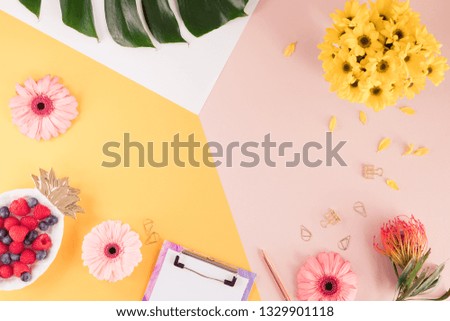 Woman business workplace with a laptop, flowers and green palm leaf on bright yellow and pink background. Top view of working space of a female at summer time. Flat lay