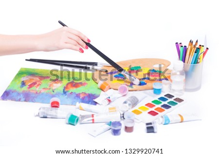 Drawing a picture, female hand close-up, stationery, paint brushes, on a white background in the studio.