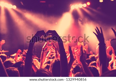 Cheering crowd at summer music festival concert and showing love sign