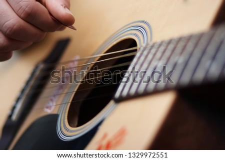 Human hand holding a mediator to play on a wooden six-string acoustic guitar, on which the drawings and stickers