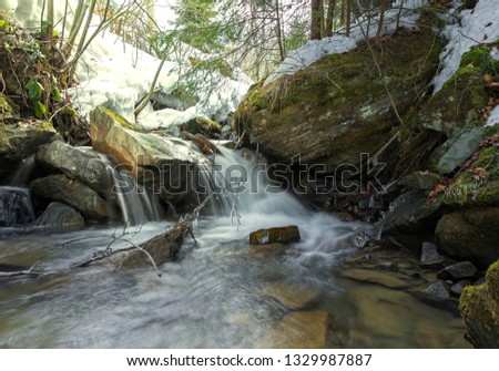 White water river and waterfalls flowing in the mountains in early spring. The mountain stream flows among stones. Early spring in the wood.  White foam on dark water, snow on the bank of a stream
