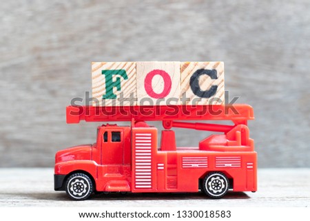 Red fire truck hold letter block in word FOC (Abbreviation of Free of charge) on wood background