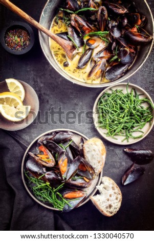 Traditional barbecue Italian blue mussel in white wine creme sauce with salicornia and baguette as top view in a casserole 