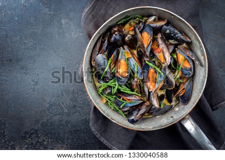Traditional barbecue Italian blue mussel in white wine creme sauce with salicornia and vegetable in as top view in a casserole Royalty-Free Stock Photo #1330040588