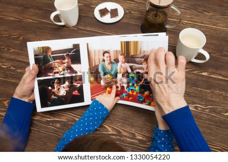 Hand senior woman and child holding a family photo album against the background of the a wooden table. Royalty-Free Stock Photo #1330054220
