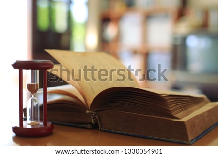 Close-up image of an hourglass on the table Old books turn into the background selective focus and shallow depth of field