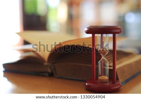 Close-up image of an hourglass on the table Old books turn into the background selective focus and shallow depth of field