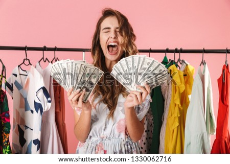 Image of fashionable girl standing near wardrobe while holding money fans isolated over pink background
