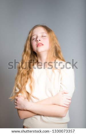 little teen girl hugs herself, studio photo over background