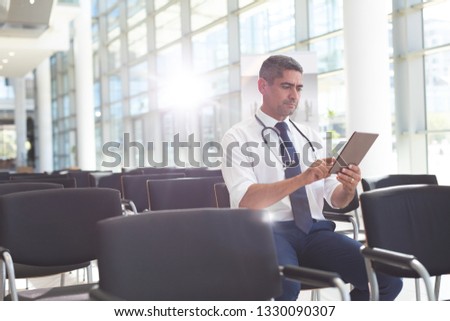 Front view of Caucasian male doctor sitting on chair and using digital tablet in conference room