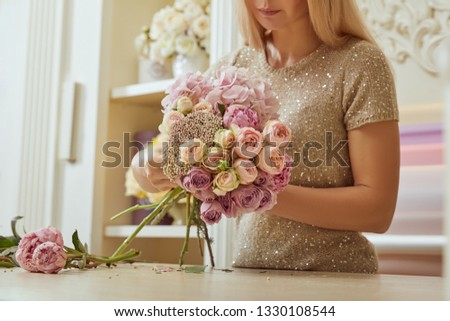 selective focus of partial view of florist making bouquet of roses and peonies at workspace