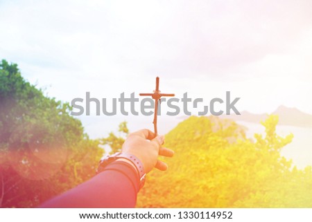 A hand is holding the Cross of Jesus with mountain background in Thailand.