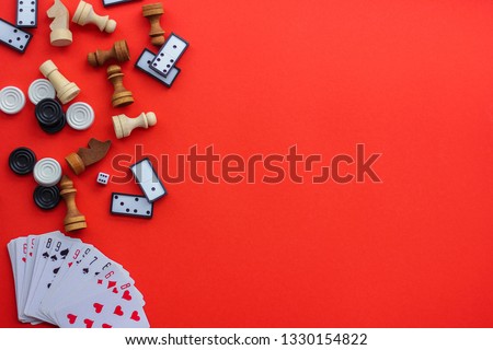 Board games on a red background: playing cards, dominoes, checkers and chess. the view from the top, place under the text