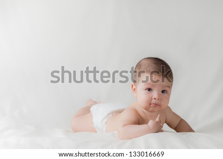 Happy cute 5 month old Asian baby boy with short black hair wearing a white cloth nappy and lying on his front on a white bed