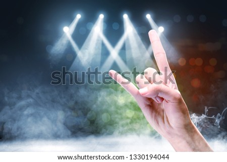 Close up view of man hand with rock gesture sign against concert spot lighting and smoke with defocused colorful lights background