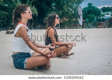 Two girlfriends doing yoga pose on beach in summertime in lotus position. Spiritually concept
