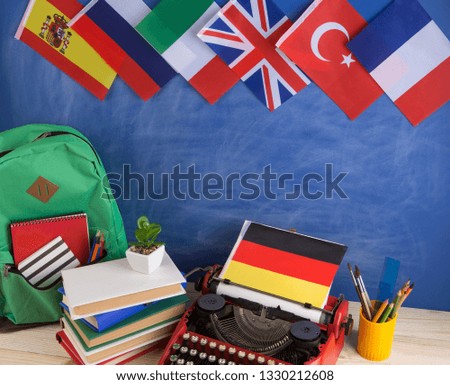 Political, news and education concept - red typewriter, flag of Germany and other countries, backpack, books, stationery on the background of the blackboard