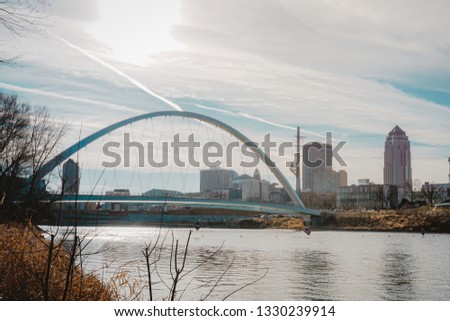 A photograph of Downtown Des Moines and the Iowa Women of Achievement Bridge from the banks of the Des Moines River in Des Moines, Iowa