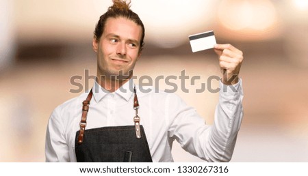 Barber man in an apron taking a credit card without money in a barber shop
