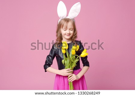 Beautiful blonde with rabbit ears holding yellow tulips and a card for a holiday gift on pink. Celebration of Easter. Concept of holidays, people and beauty.