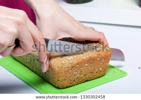 Baking bread at home. A loaf of freshly baked wholegrain bread with sunflower seeds lies on a cutting board. A woman cuts it with a knife.