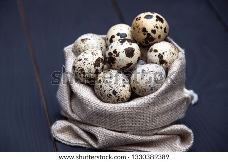Quail eggs in fabric bag on black wooden background. Easter holiday.