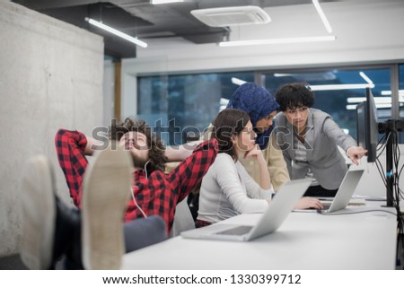 young software developer resting with legs on desk while his multiethnics business team writing programming code in the background at startup office