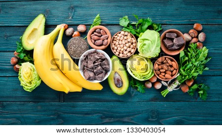 Foods containing natural magnesium. Mg: Chocolate, banana, cocoa, nuts, avocados, broccoli, almonds. Top view. On a blue wooden background. Royalty-Free Stock Photo #1330403054