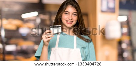 Girl with apron holding a credit card in a bakery