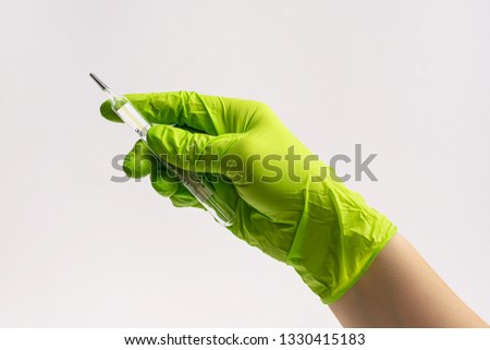 Doctor’s hand in green rubber glove holding glass thermometer on white background.