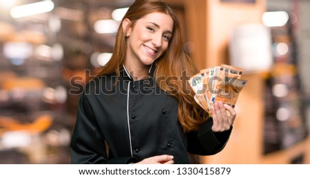 Young redhead chef woman holding an empty placard for insert a concept in the bakery