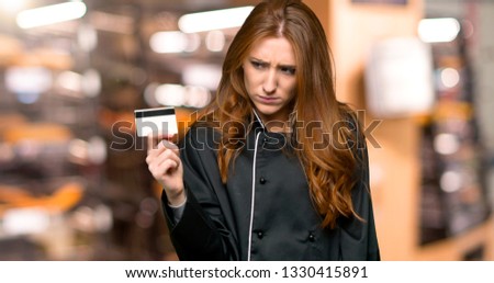 Young redhead chef woman taking a credit card without money in the bakery