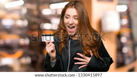 Young redhead chef woman holding a credit card and surprised in the bakery
