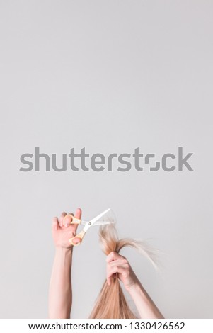 Young woman cutting her long blond hair with scissors. Image with copy space.