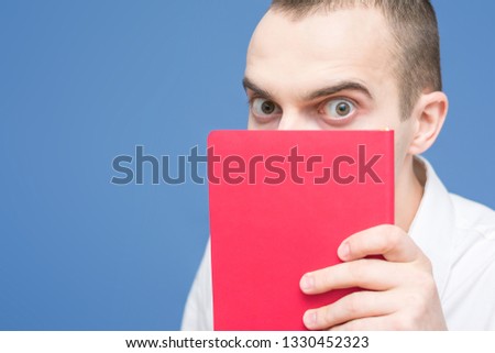 Student in the white shirt with red book, book of horrors, peeking out from behind the book, with horror looking at the camera, close up