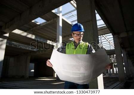 Young architect analyzing blueprint of the building at the construction site