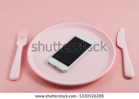 smartphone with the screen facing up lying on the pink plate with the devices on pink background
