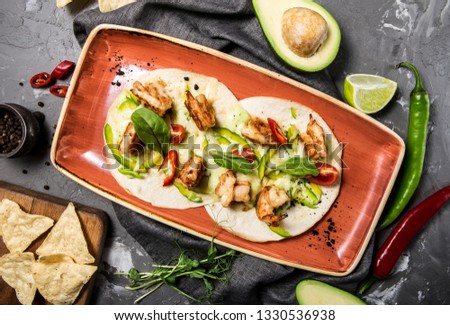 Mexican taco dish with shrimps, bell peppers, tomatoes and chili peppers on a concrete gray background