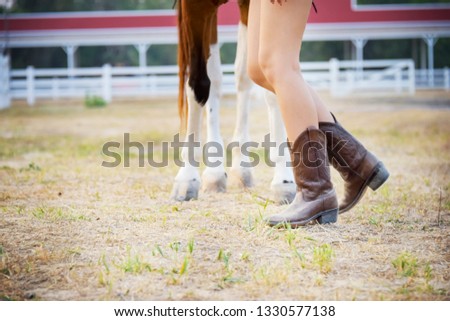 Legs of cowgirl walking with horse. Farmer girl in countryside ranch. Beautiful woman training and taking care of her horse with love and caring.