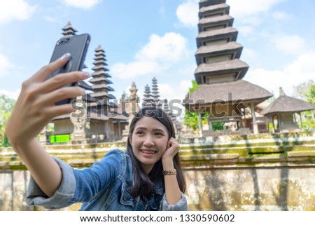 Happy young woman taking selfie. Technology traveling concept.
Asian tourist girl takes selfie on vacation at Pura Taman Ayun temple, village of Mengwi Badung worship royal family in Bali, Indonesia.