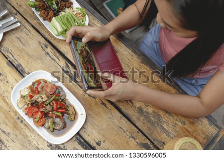 Asian woman is taking a photo of Thai food on the table.