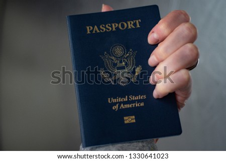 Female hand holding Passport of USA on blurred silver background. 