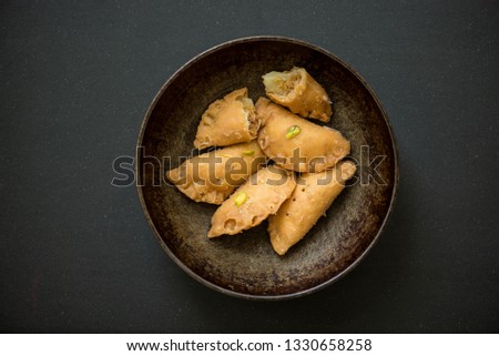 A traditional Indian sweet Gujia or Karanji served in a rustic, old pan on a dark background. Indian authentic sweet or dessert.